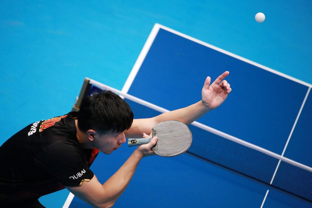 A beginner player hits a forehand in a game of table tennis. The ball is in mid-air, and the player is focused on their shot.